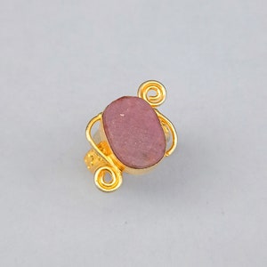 May include: A gold ring with a pink oval-shaped stone set in a wire design.