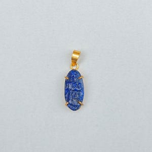 May include: A gold pendant featuring a blue lapis lazuli stone with a carved design. The stone is oval shaped and set in a gold frame.