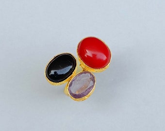 May include: A gold ring with three oval-shaped gemstones. The stones are red, black, and purple.