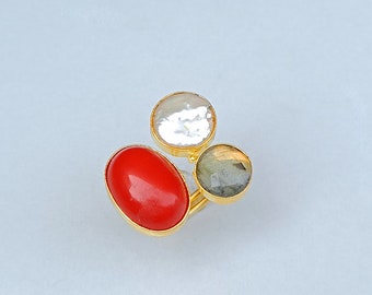 May include: A gold ring with three stones: a red oval, a white round, and a gray round.