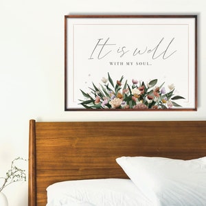 May include: A framed print featuring a floral design and the text "It is well with my soul." The print is hanging on a white wall above a wooden headboard.