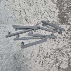 Könnte beinhalten: Ein Satz mit sechs grauen Metall-Schrankgriffen. Die Griffe sind rechteckig mit einer leichten Biegung oben und unten. Sie liegen alle auf einer grauen, strukturierten Oberfläche.