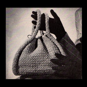 Pode incluir: Uma bolsa de mão de crochê cinza com um design descontraído e duas alças. A bolsa está sendo segurada por uma mão.