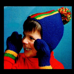 May include: A blue knitted hat with a colourful striped band and a pom-pom on top. The hat is being worn by a child wearing a red sweater and blue mittens with colourful stripes.