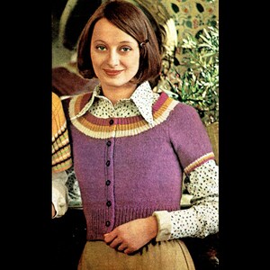 May include: A purple knitted cardigan with a multi-coloured stripe around the neckline. The cardigan has a button closure and short sleeves.
