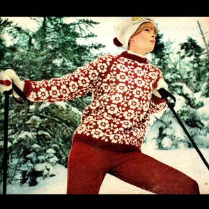 May include: A woman wearing a red and white knitted sweater with a floral pattern, red pants, and a white knit hat. She is holding ski poles and is standing in a snowy forest.