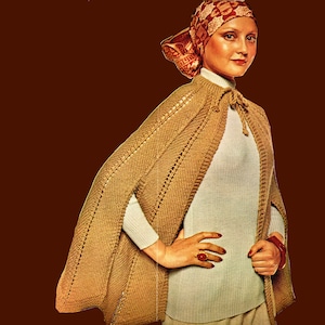 May include: A brown knitted cape with a white turtleneck sweater underneath. The cape has a decorative tie at the neck and is worn with a patterned headscarf.