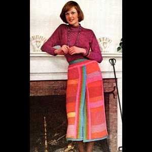 May include: A woman wearing a long, colorful, crocheted skirt with a pink, orange, yellow, green, and blue striped pattern. She is also wearing a purple turtleneck sweater and a long, beaded necklace.