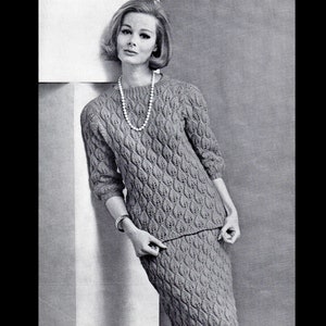 May include: A knitted sweater and skirt set in a gray color with a textured pattern. The sweater has a round neckline and three-quarter sleeves. The skirt is knee-length.