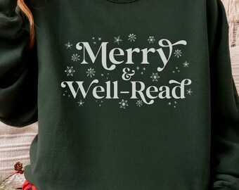 Può includere: Una felpa verde scuro con la scritta bianca "Merry & Well-Read", decorata con dettagli a forma di fiocco di neve. La felpa è a girocollo. La persona nell'immagine indossa pantaloni del pigiama a quadri rossi e neri.