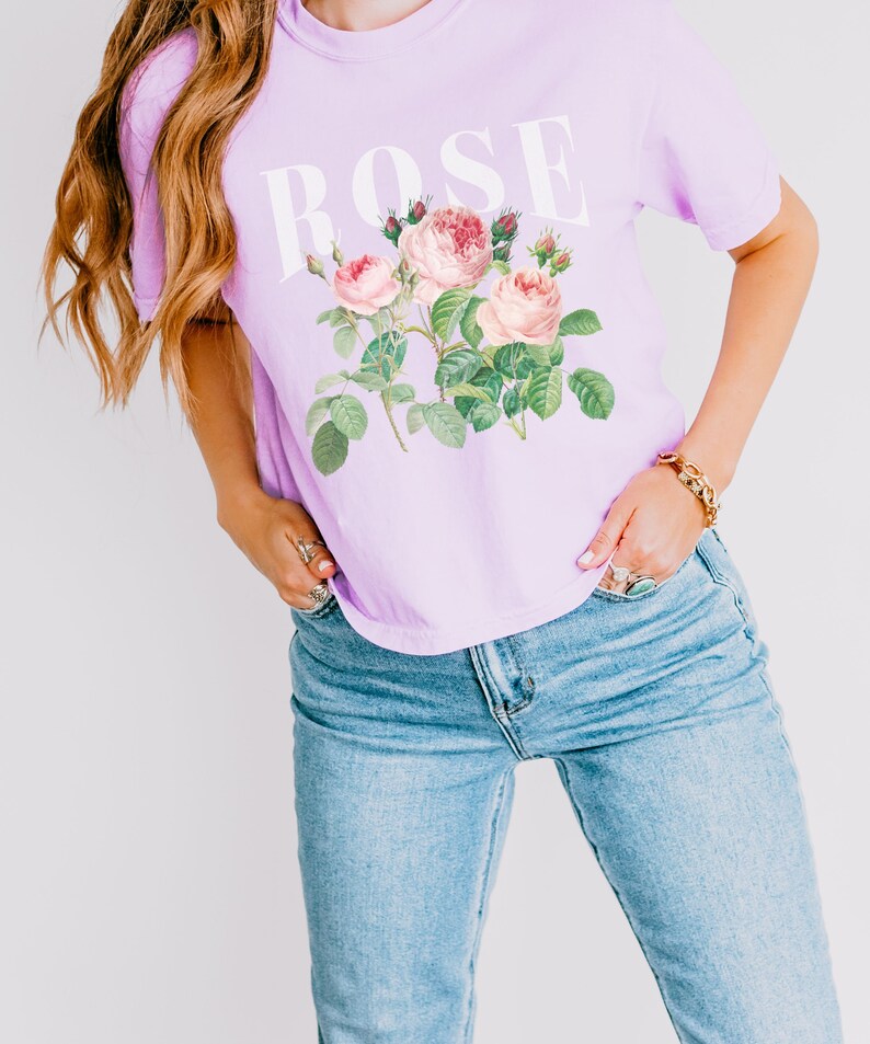 May include: A lavender t-shirt featuring a graphic of pink roses and the word "ROSE" printed in white.