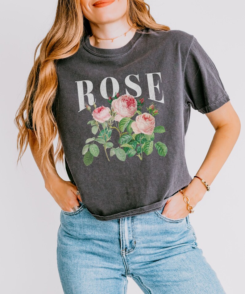 May include: A dark grey t-shirt with a vintage-style floral print of pink roses and green leaves. The word "ROSE" is printed in white above the floral design.