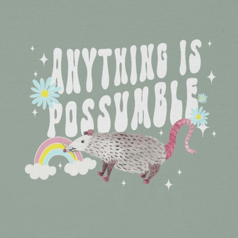 May include: A light green graphic featuring a possum, rainbow, and daisies. The text "ANYTHING IS POSSUMBLE" is written in white, retro-style lettering. The possum is gray with a pink tail and feet.