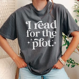 May include: Dark gray t-shirt with the text "I read for the plot" in white, with star accents. The shirt is a casual style, suitable for everyday wear.