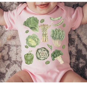May include: A pink baby onesie with a green vegetable print. The vegetables include broccoli, asparagus, artichoke, cabbage, bell pepper, and spinach.