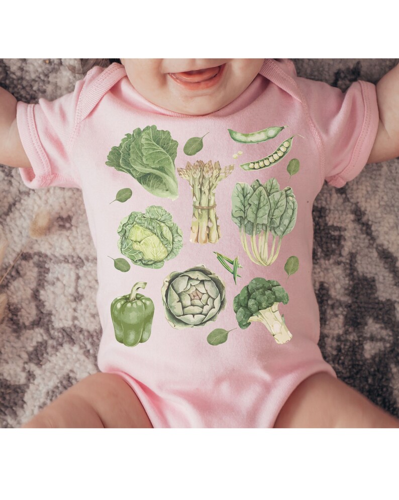 May include: A pink baby onesie with a green vegetable print. The vegetables include broccoli, asparagus, artichoke, cabbage, bell pepper, and spinach.