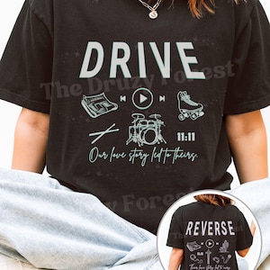 Peut inclure: T-shirt noir avec le mot "DRIVE" en blanc. Le design comprend des illustrations d'un clavier, d'un bouton de lecture, d'un patin à roulettes et d'une batterie. Le texte "Our love story led to theirs" est également présent. Le dos du t-shirt dit "REVERSE".