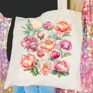 May include: A white tote bag with a floral design featuring pink, peach, and white peonies. The flowers are arranged in a cluster and have green leaves.
