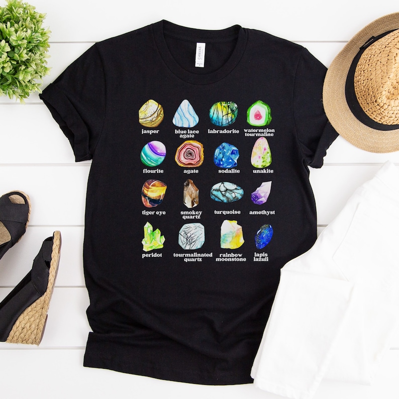 Op de afbeelding: Zwart T-shirt met een afbeelding van verschillende soorten edelstenen, waaronder jaspis, agaat, sodaliet, amethist, peridoot en lapis lazuli.