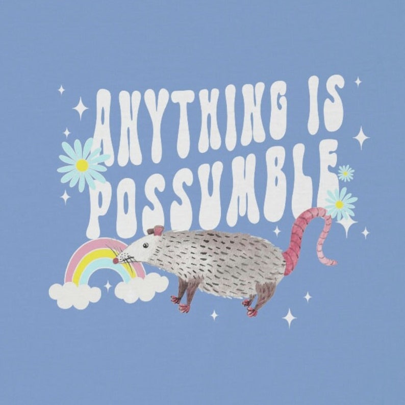 May include: A light blue graphic featuring a possum with a rainbow, daisies, and stars. The text reads "ANYTHING IS POSSUMBLE" in white, retro-style lettering. The possum is gray with a pink tail and feet.