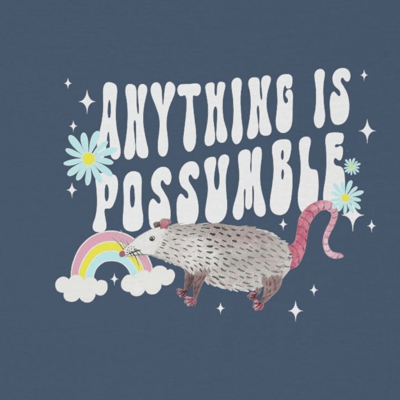 May include: A navy blue graphic design featuring a possum, rainbow, and daisies. The text "ANYTHING IS POSSUMBLE" is written in white, retro-style lettering. The possum is gray with a pink tail and feet.