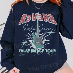 Peut inclure: Sweat-shirt bleu marine avec un graphisme comportant le mot "R3V3RB" en rouge et blanc, et le texte "Easton Crowne". Une guitare turquoise est au centre, avec les mots "FALSE IMAGE TOUR" en dessous. Les noms LL Garrison, Syd Patel et Tack Garrett sont également inclus.