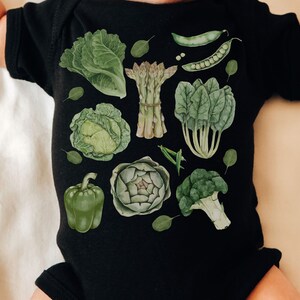 May include: A black baby onesie with a green and white print of various vegetables, including asparagus, broccoli, artichoke, cabbage, spinach, and peppers.