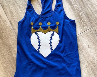 Puede incluir: Un top de tirantes azul real con un corazón de béisbol blanco y una corona de purpurina dorada en la parte superior.