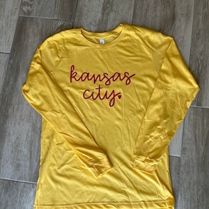 May include: A yellow long-sleeved t-shirt with the words "kansas city" written in red on the front.