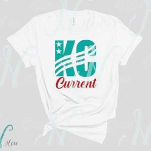 May include: White t-shirt with a teal blue graphic of the letters "KC" with stars and stripes. The text "Current" is written in red below the graphic.