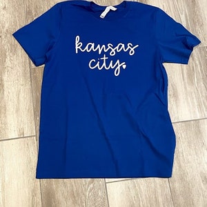 May include: A royal blue t-shirt with the text "kansas city" in white cursive lettering.