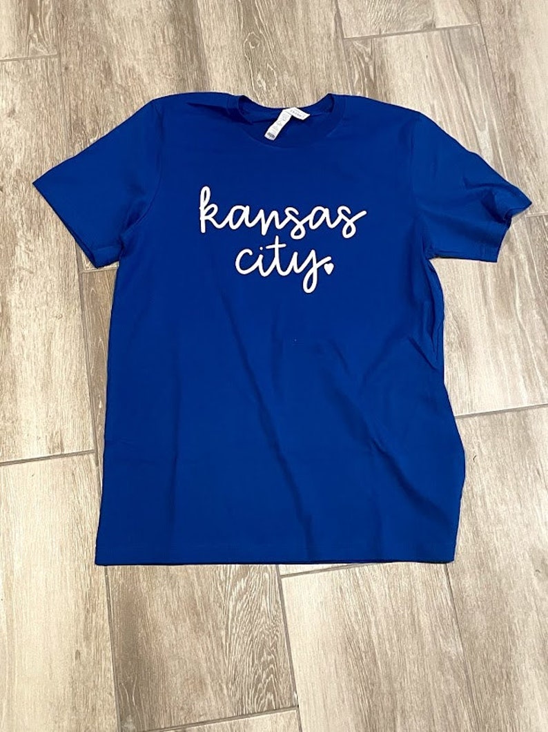 May include: A royal blue t-shirt with the text "kansas city" in white cursive lettering.