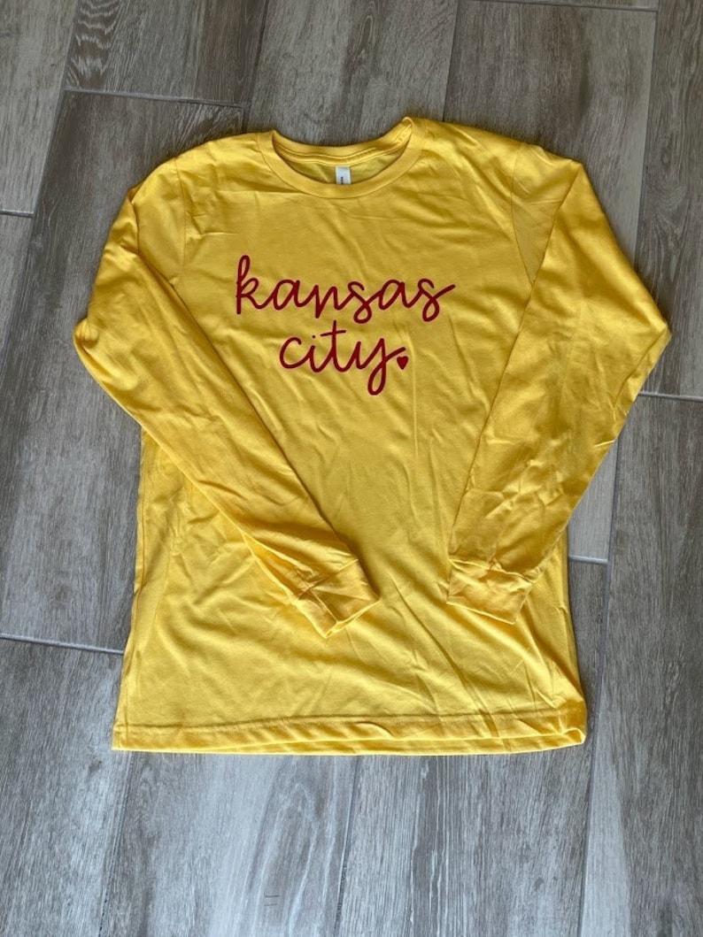 May include: A yellow long-sleeved t-shirt with the words "kansas city" written in red on the front.
