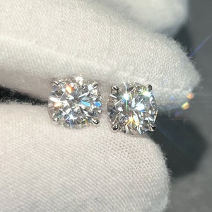 Könnte beinhalten: Ein Paar runde, klare Diamant-Ohrstecker. Die Ohrringe sind in einer silbernen Metallfassung gefasst.