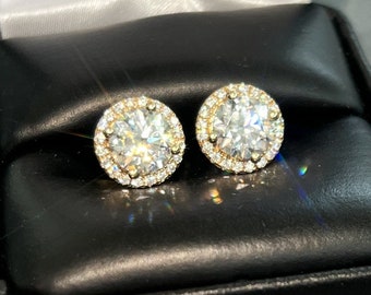 May include: A pair of gold earrings with a round, clear diamond center stone surrounded by a halo of smaller diamonds.