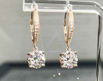 May include: A pair of gold dangle earrings with a round, clear stone and a row of smaller clear stones on the drop.