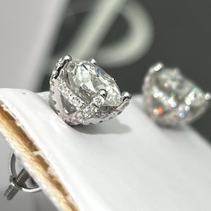 May include: A pair of silver earrings with a large, clear, pear-shaped gemstone set in a silver prong setting. The gemstone is surrounded by a halo of smaller, clear gemstones.