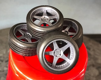 May include: Four silver and black model car wheels stacked on top of each other on a red surface.