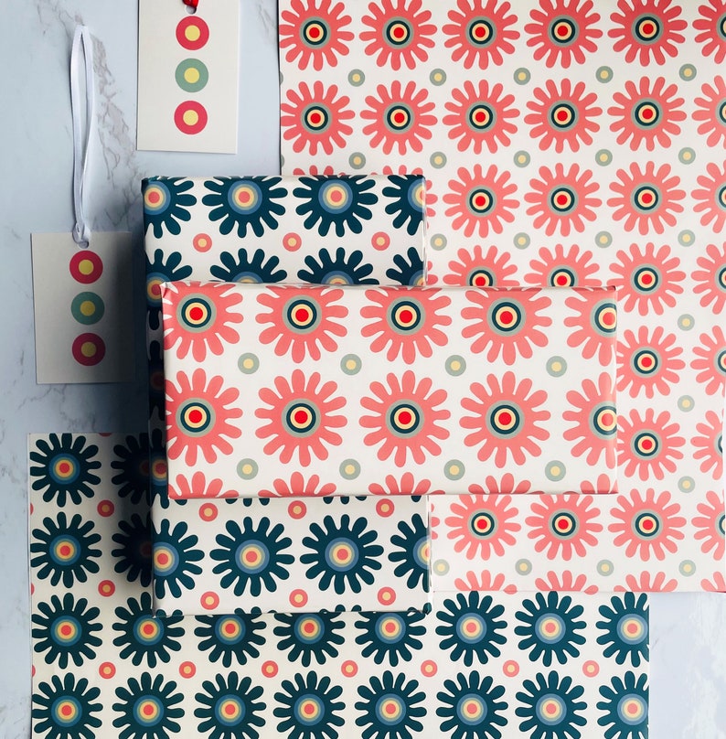 May include: A stack of wrapping paper featuring different patterns of colorful flowers and circles. The wrapping paper is in shades of pink, red, blue, green, and yellow.