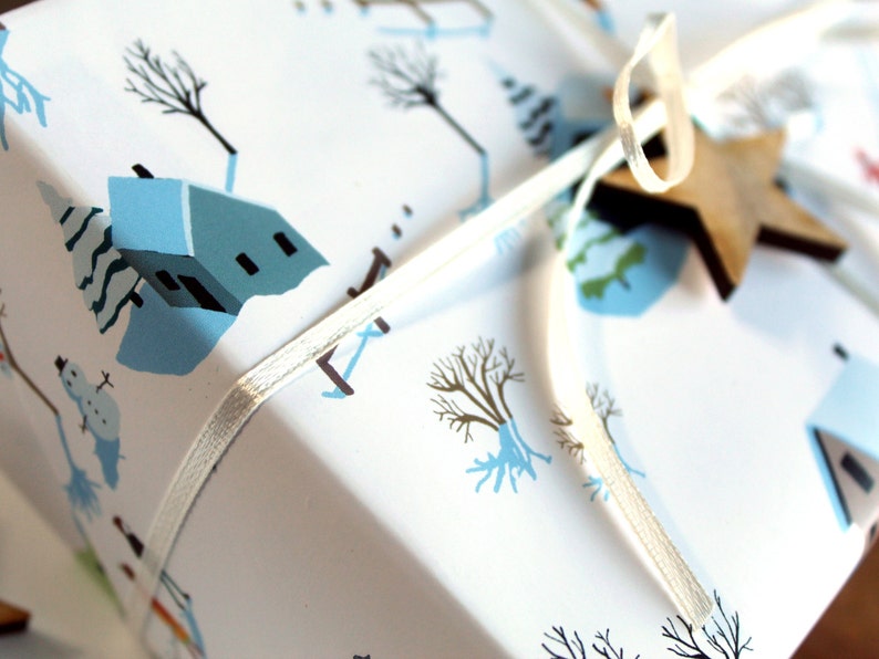 May include: A white gift box wrapped in paper featuring a winter scene with light blue houses, bare trees, and snowmen. The package is tied with a thin white ribbon and decorated with a small, flat, five-pointed wooden star ornament.