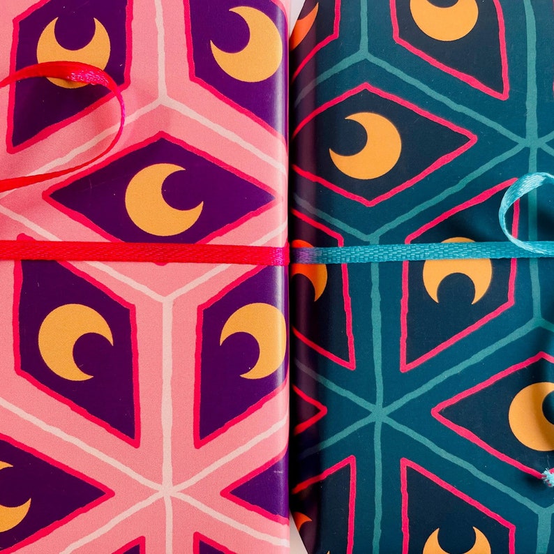 May include: Two wrapped gifts with patterned paper. One is pink and purple with a crescent moon design, tied with a red ribbon. The other is teal and navy with a similar design, tied with a teal ribbon. The gifts are side by side.
