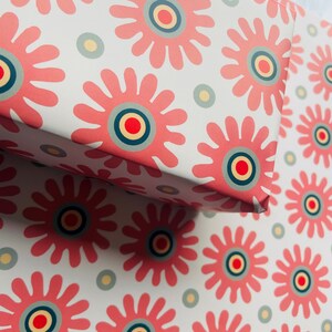 May include: Pink and white wrapping paper with a repeating pattern of stylized pink flowers with a concentric circle design in the center. The circles are red, yellow, and blue.