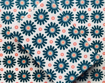 May include: White wrapping paper with a repeating pattern of blue and red stylized flowers. The flowers have a white center and are surrounded by a white ring.
