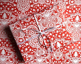 May include: A wrapped gift with a red background and a white lace-like pattern of stars, hearts, and Christmas trees. The gift is tied with a silver ribbon. The wrapping paper is also used as the background.