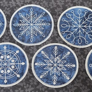 May include: Six blue and white snowflake-themed coasters. The coasters are round and have a white snowflake design on a blue background.