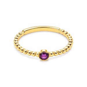 Peut inclure: Une bague en or avec un anneau perlé et une pierre précieuse violette ronde. La bague a une section lisse et plate sur le dessus. Un bijou délicat.