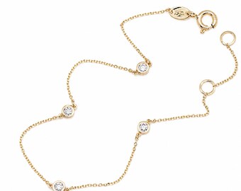 May include: A delicate gold chain bracelet featuring four evenly spaced round clear stones set in gold bezels. The bracelet includes a circular spring ring clasp and a small oval tag near the closure, showcasing a refined and minimalist design.