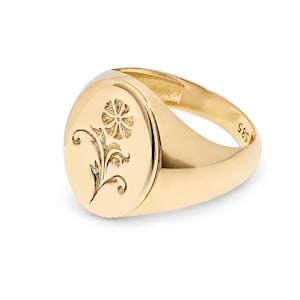 May include: A polished gold signet ring featuring an oval face with an engraved floral design. The interior of the band is clearly stamped with the number 585, indicating the gold purity. The ring has a smooth, reflective surface and a solid band.