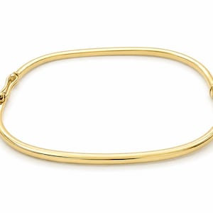 Può includere: Un bracciale rigido in oro giallo lucido con un profilo liscio e arrotondato. Il bracciale presenta un meccanismo di chiusura a cerniera sicuro su un lato e una piccola articolazione a cerniera arrotondata sul lato opposto, creando una forma ovale.