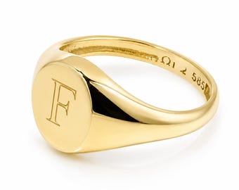 Puede incluir: Un anillo de sello de oro pulido con una cara circular grabada con la letra F. El interior de la banda muestra el sello 585, que indica la pureza del oro. El anillo tiene una superficie lisa y reflectante con un diseño de banda redondeada.